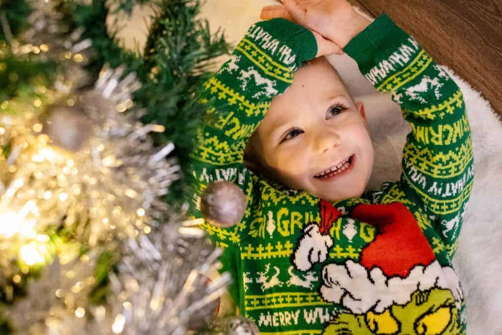 Young boy smiling while lying under Christmas tree. Unique In-Home Christmas Mini Shoots by Rebecca Morgan Photography 