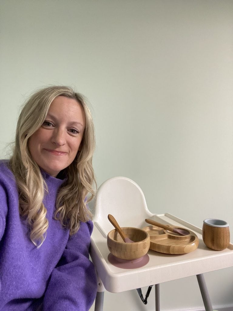 Lady sitting in front of a high chair with toddler bowls, plates and cutlery on it. Nutrition with Caz on Northants Families website.