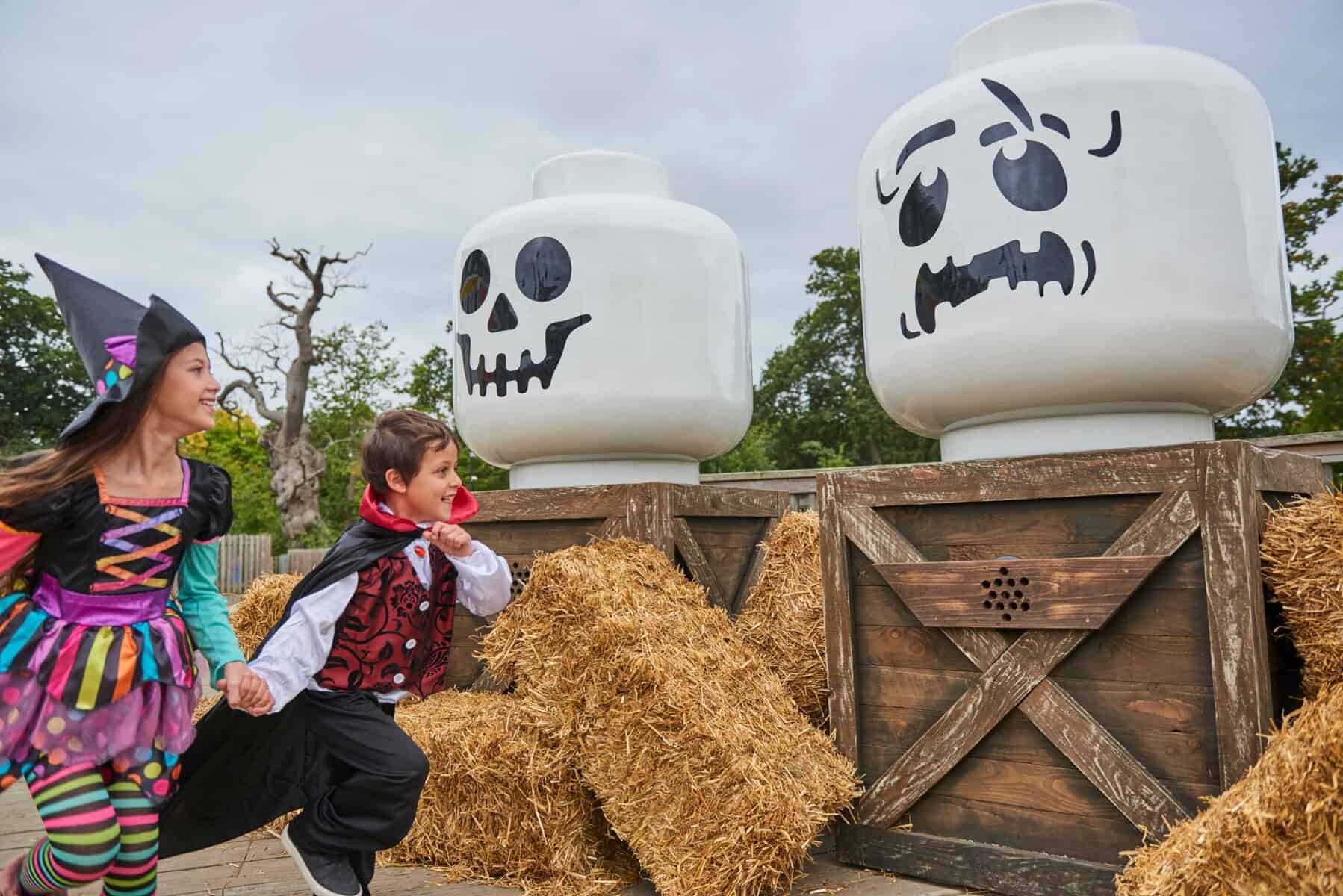 Child dressed in vampire costume running in front of giant skeleton lego heads. Northants Families
