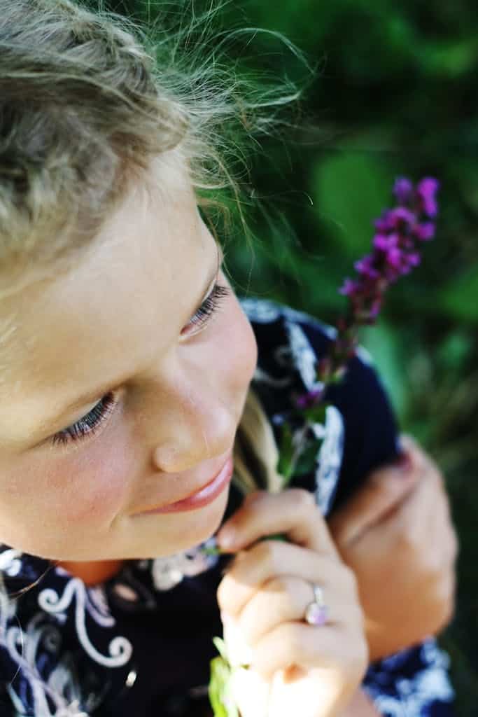 Charming portrait of a young girl with blonde hair holding a purple flower outdoors.