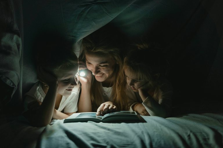 Mum and children reading a book by torchlight under blankets. Screen free time. Northants Families