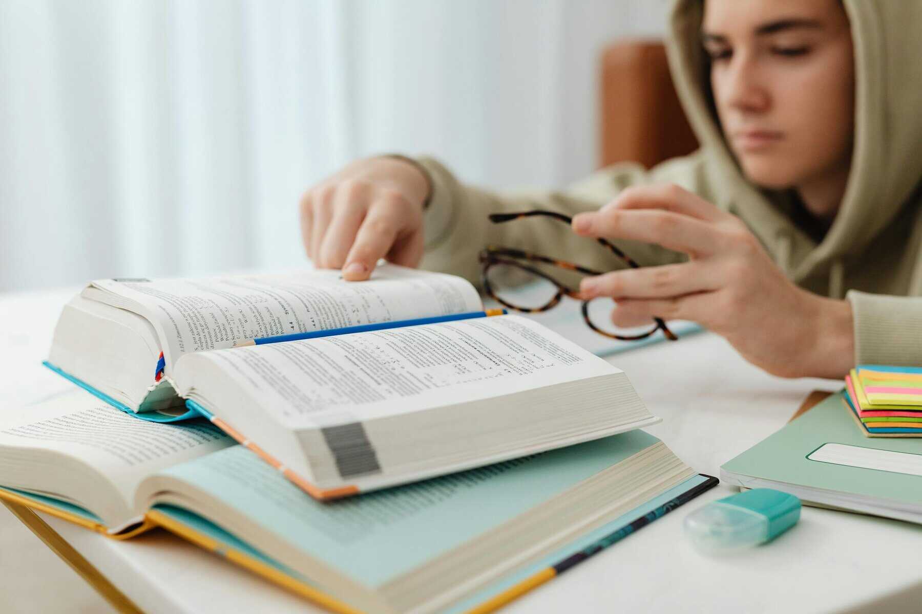 Focused teenager studying with open textbooks, eyeglasses, and notes.