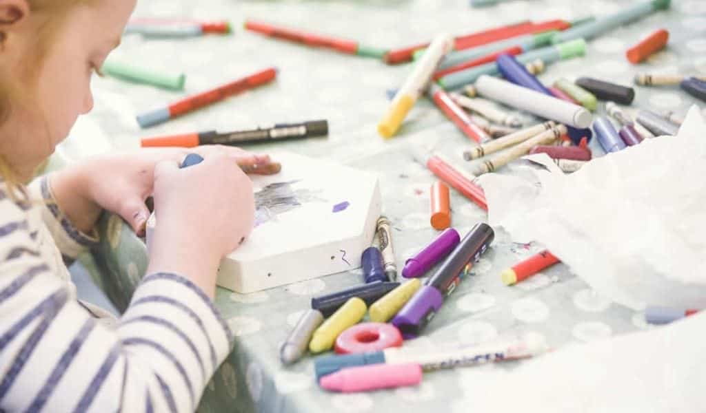 Young child colouring with colourful pens and crayons spread over table