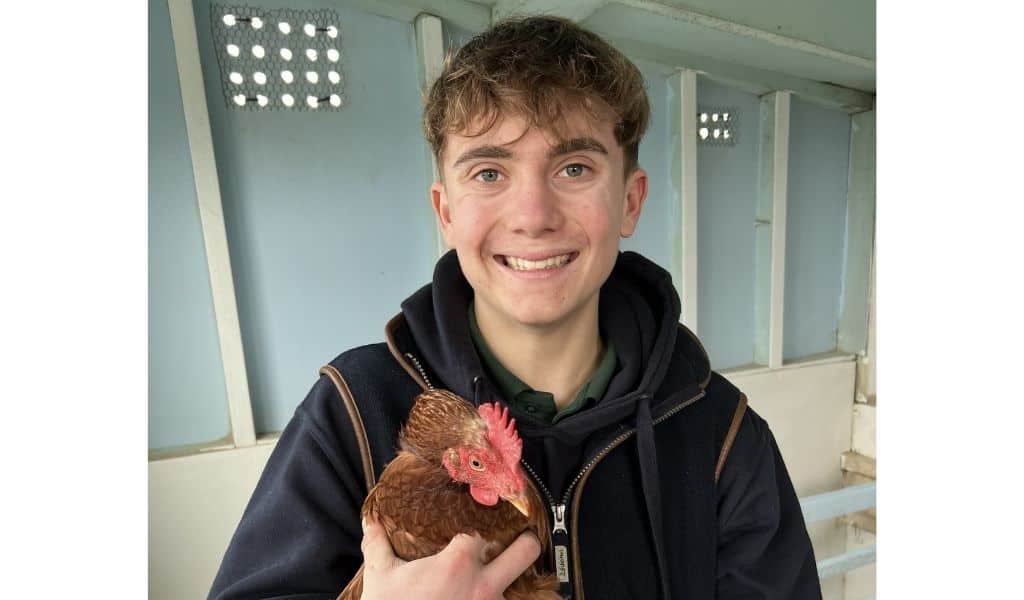 Tom Wells, previous NAS Youth Plotter Ambassador, holding a chicken on a farm