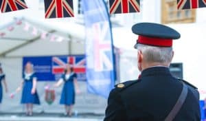 Military officer in dress uniform watching a stage performance with Union Jack bunting at an Armed Forces Day event in Northampton Market Square