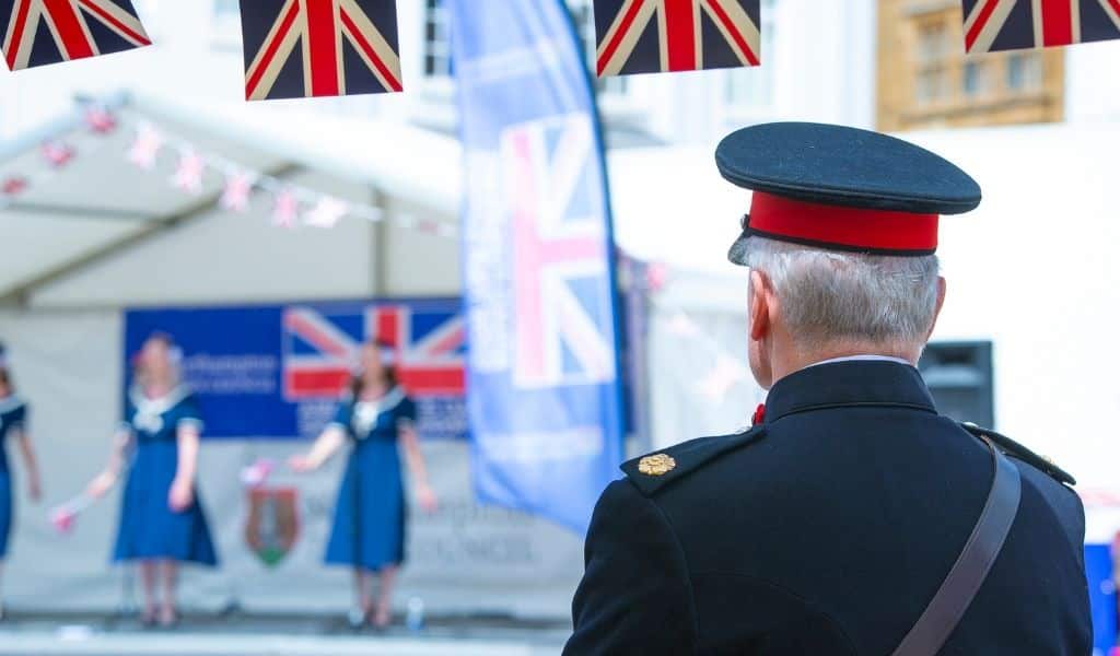Military officer in dress uniform watching a stage performance with Union Jack bunting at an Armed Forces Day event in Northampton Market Square