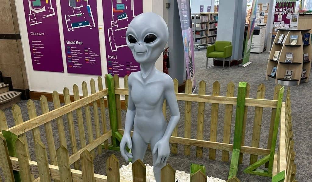 Model of a white alien standing within a fenced area at the local library