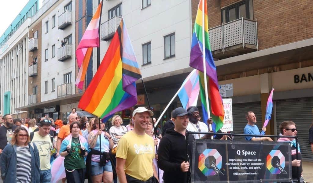 People walking through town in a Pride event. Carrying pride flags