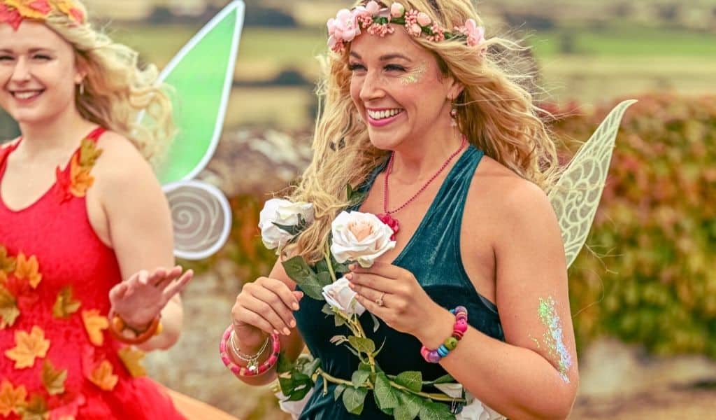 A lady with long blonde wavy hair dressed as a fairy and holding a flower