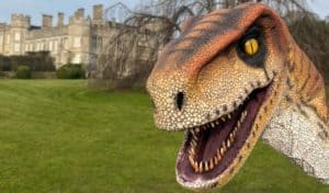 Close-up of an animatronic raptor puppet on the lawn at Deene Park, alongside the Dinosaur Day ticket booking options