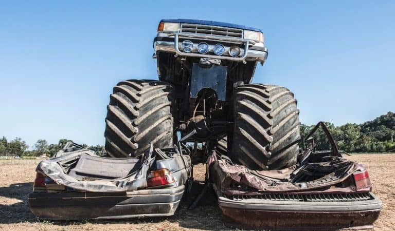 A monster truck with giant wheels crushing two cars beneath it at an outdoor event.