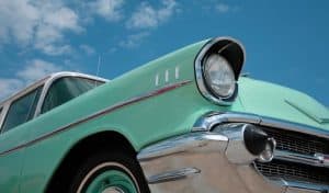 Close-up of a mint green vintage classic car with chrome detailing, parked outdoors against a blue sky with clouds.