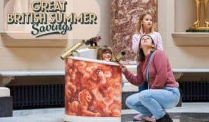 Mother and two daughters looking through a brass telescope prop inside the Marble Saloon at Stowe House, promoting the Great British Summer Savings discounted admission offer
