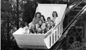 Black and white archive photo from the 1970s showing a group of women and children laughing and screaming with excitement as they ride down Wicksteed Park's Water Chute towards the splashdown