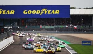 Endurance racing cars lined up on the grid at the start of a race at Silverstone, with a large Goodyear sign above the pit straight and spectators in the grandstands.