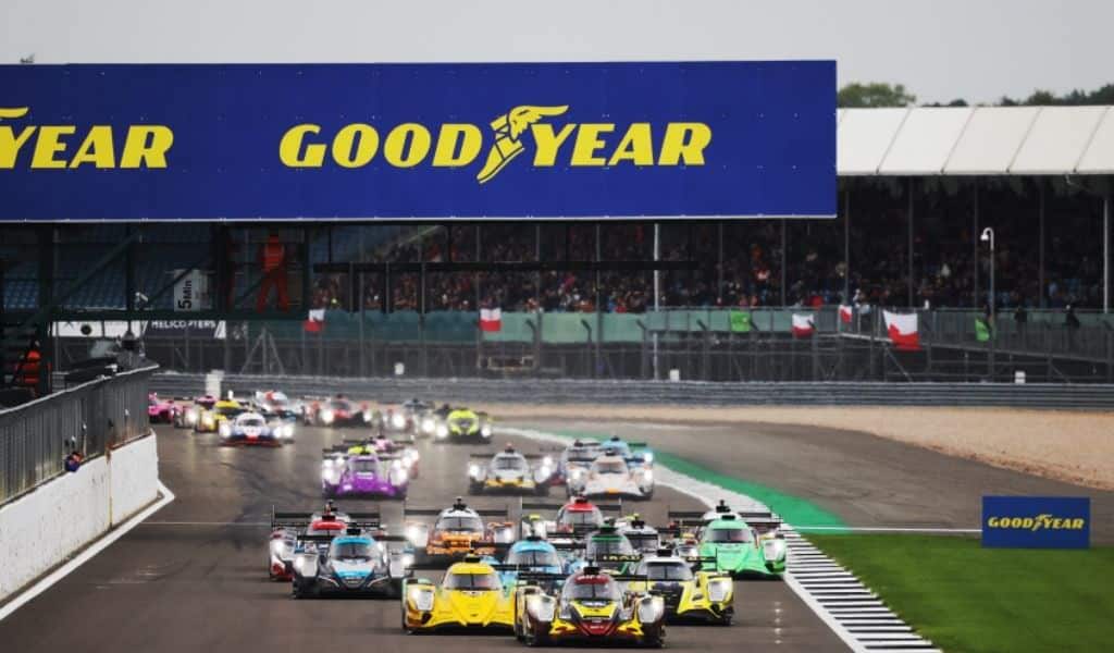 Endurance racing cars lined up on the grid at the start of a race at Silverstone, with a large Goodyear sign above the pit straight and spectators in the grandstands.